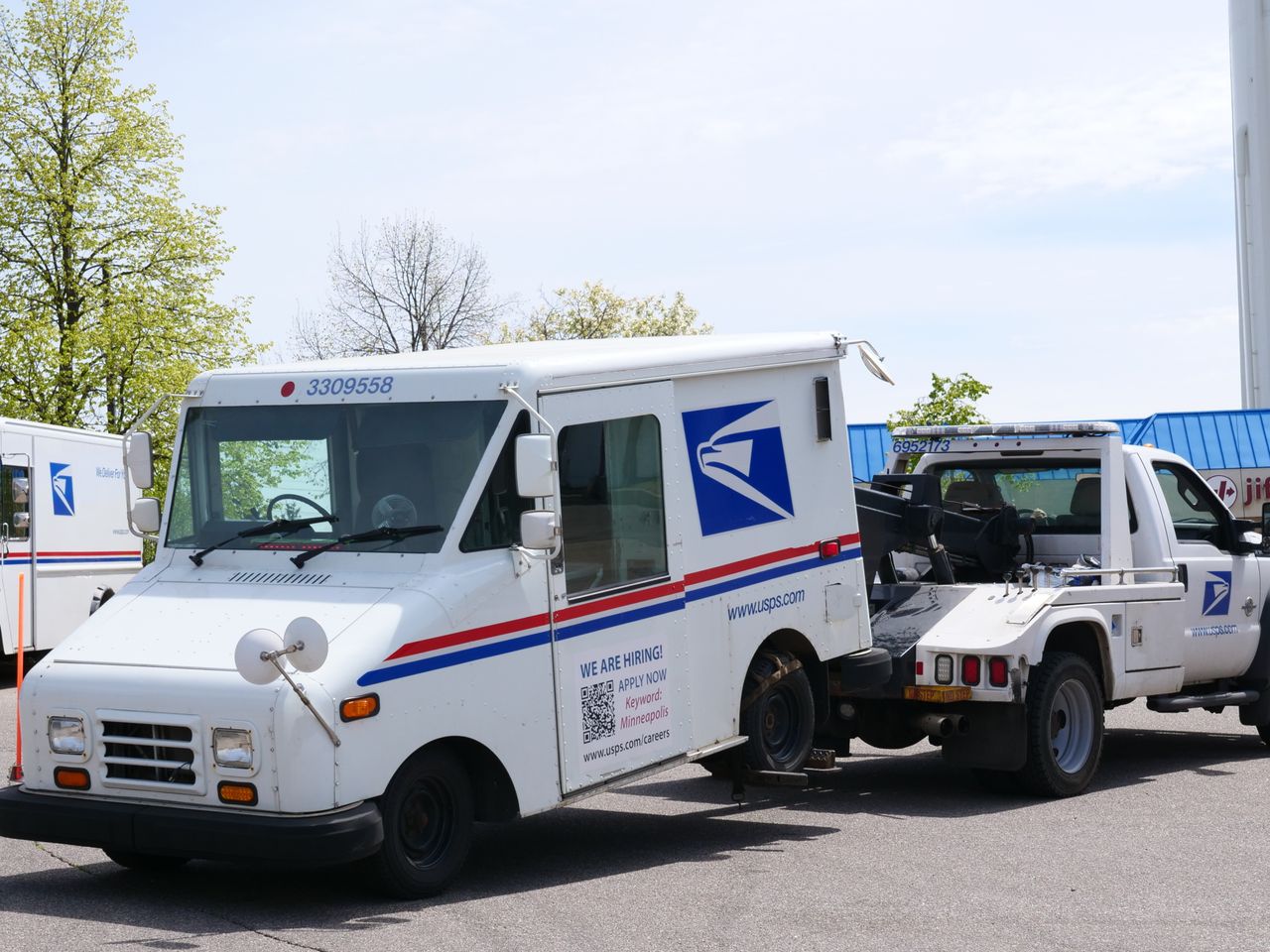 A United States Postal Service (USPS) mail truck is being towed outdoors on a clear day.